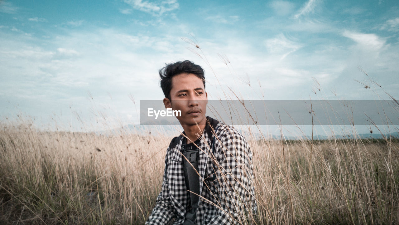 Portrait of young man standing on field against sky