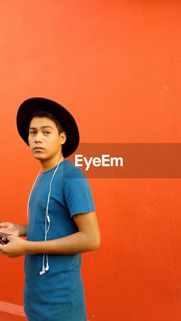 Portrait of young man in hat standing against orange wall