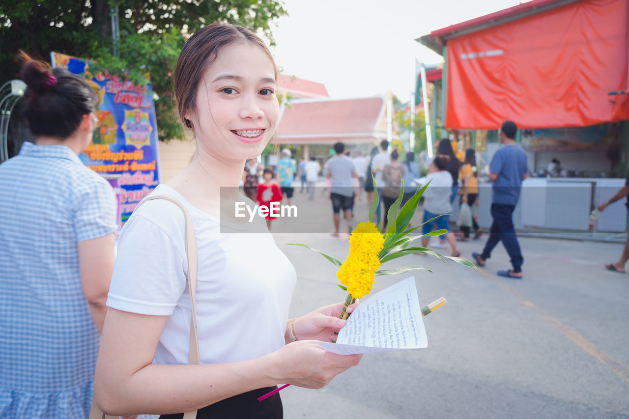 Portrait of smiling woman with flowers and paper standing on street