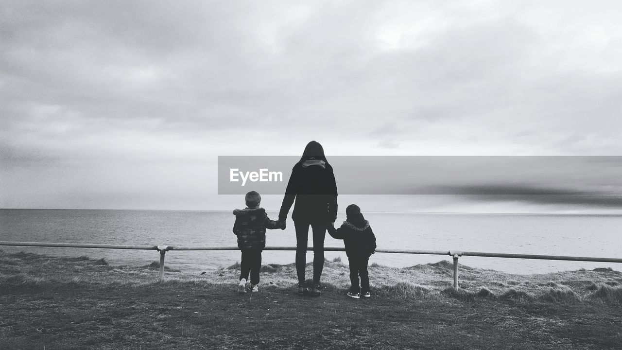 Rear view of mother with sons standing at beach against sky