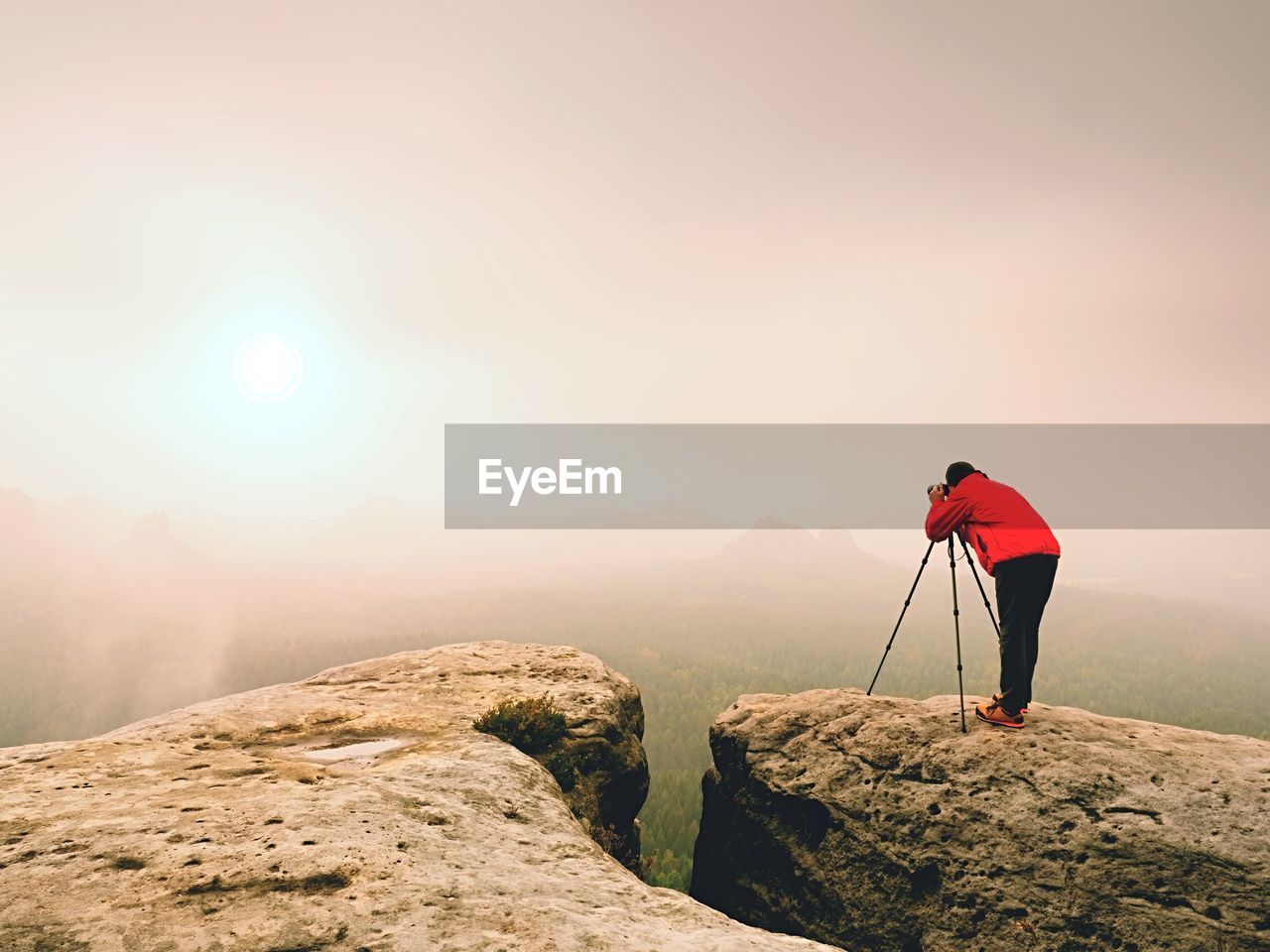 REAR VIEW OF MAN STANDING ON ROCKS AGAINST SKY