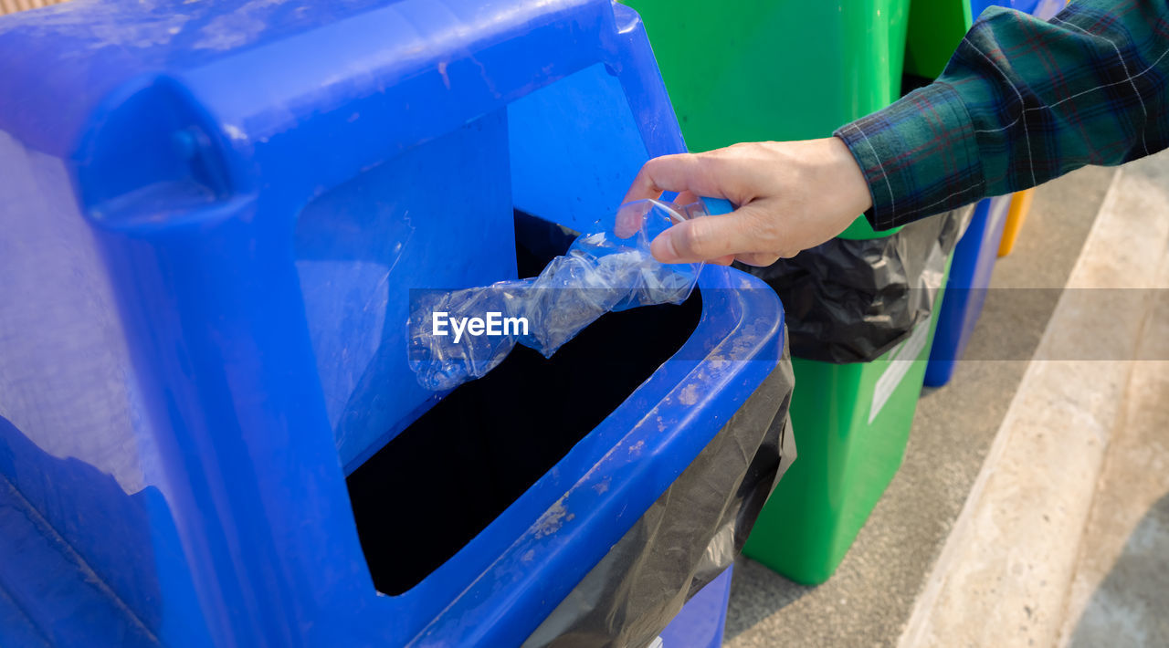 People hand throwing empty water bottle in recycle bin. blue plastic recycle bin. man discard water