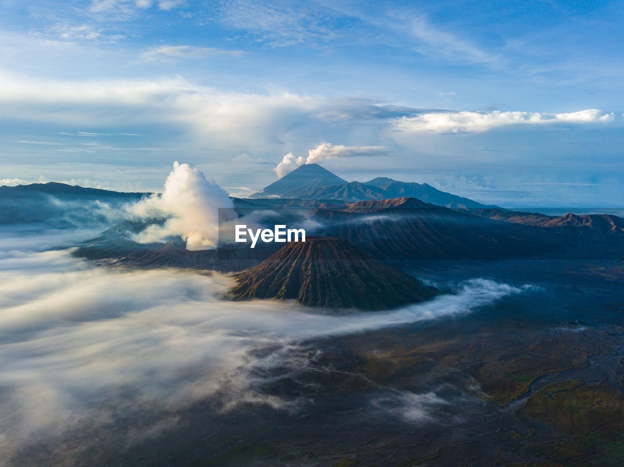 Smoke emitting from volcanic mountains against cloudy sky