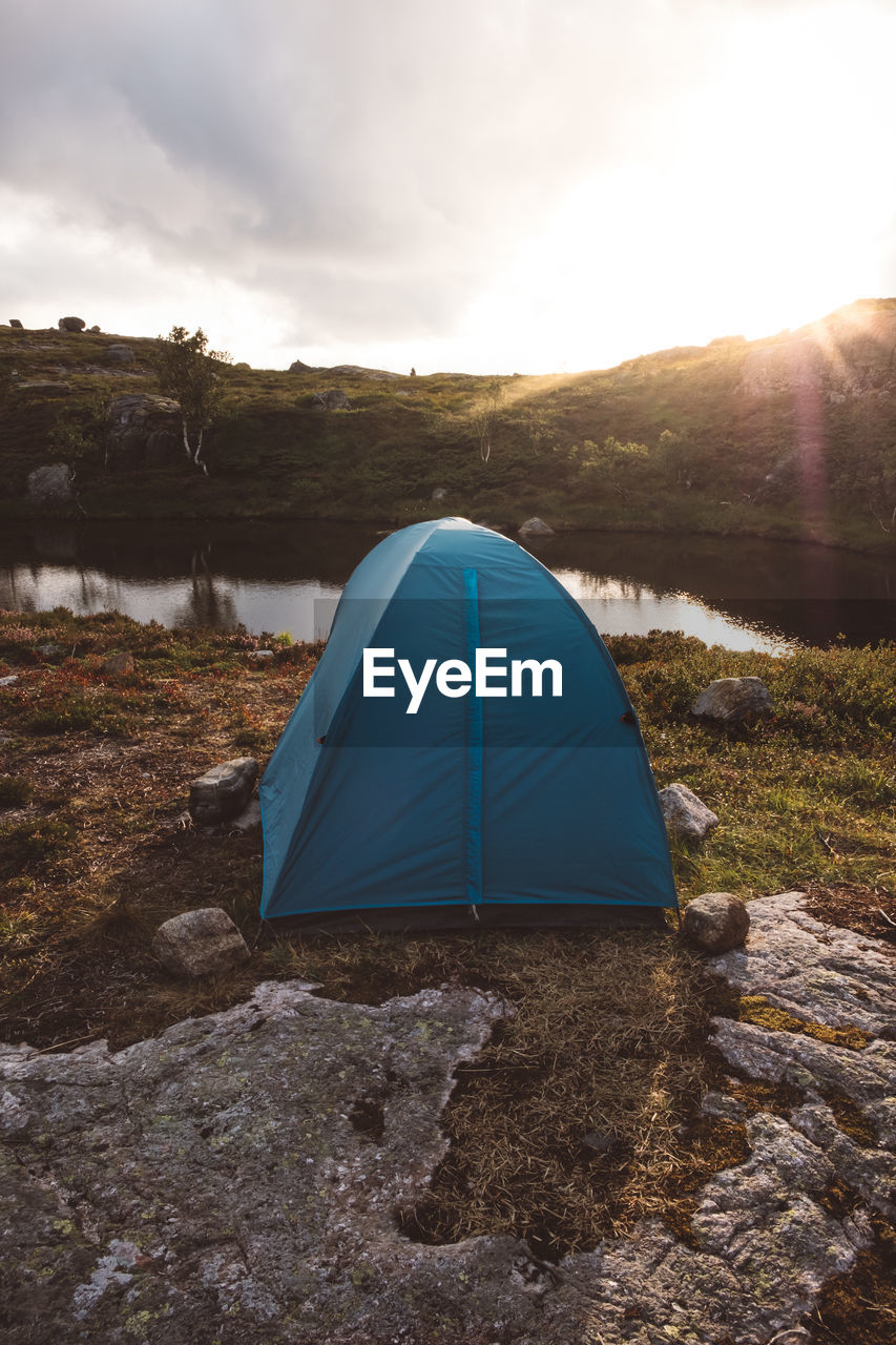Tent near a lake against cloudy sky and sunset