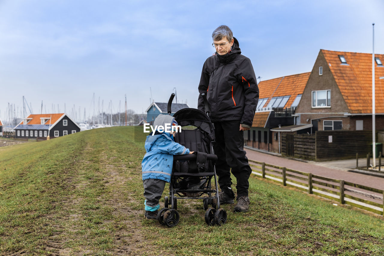 Grandfather standing by granddaughter on field against house