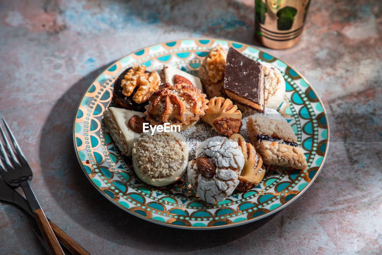 From above of baklava and biscuits with moroccan peppermint tea near knife and fork placed on table decorated with mint leaves