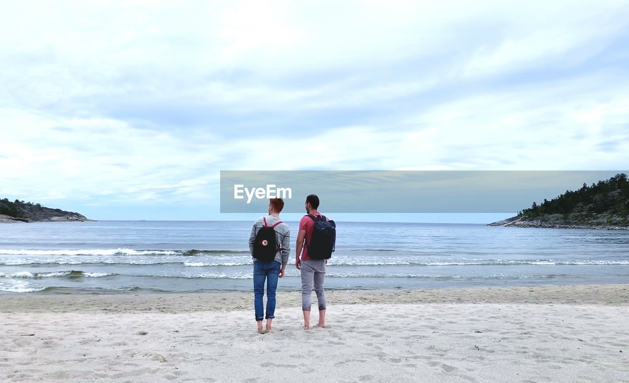 FRIENDS STANDING ON BEACH AGAINST SEA