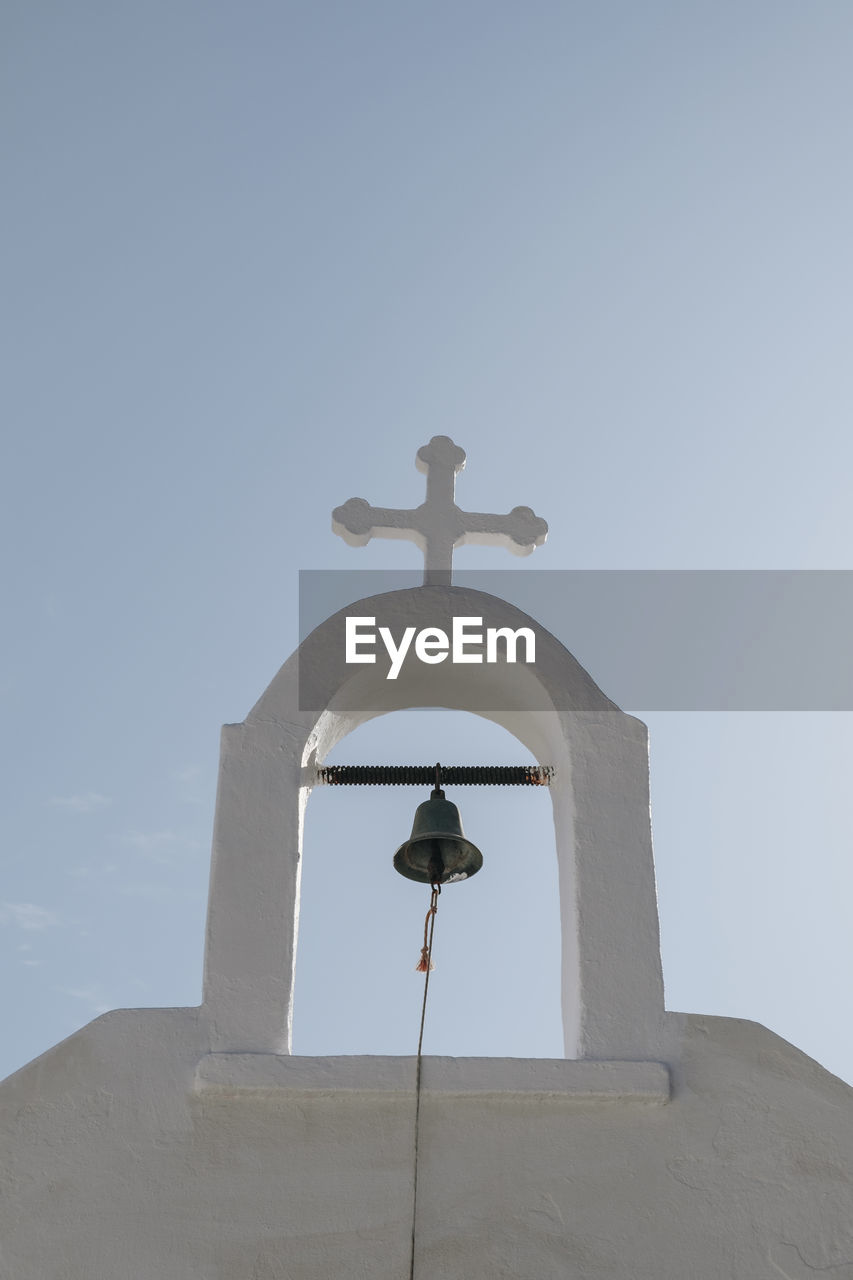 Low angle view of the bell and cross on a church in ana mera, mykonos, greece.