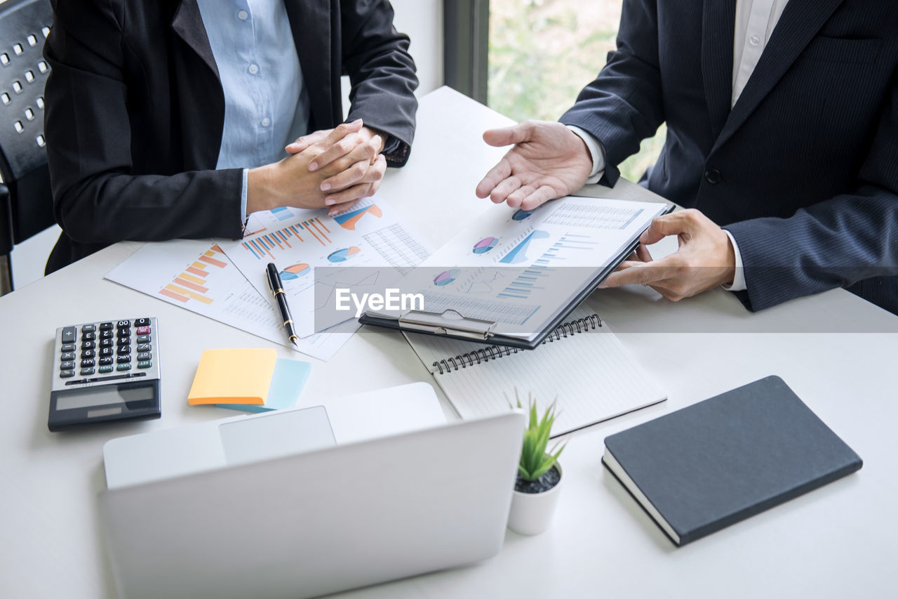 Midsection of and businessman and colleague discussing over graph on table