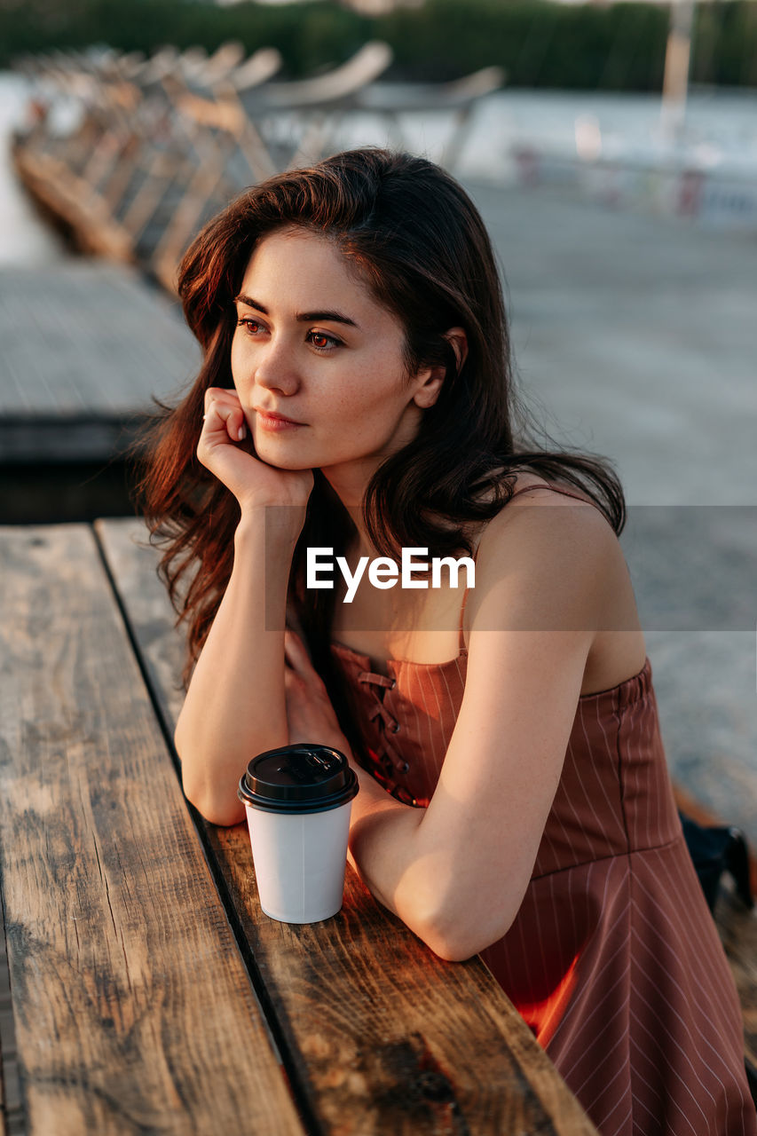 YOUNG WOMAN SITTING WITH COFFEE CUP