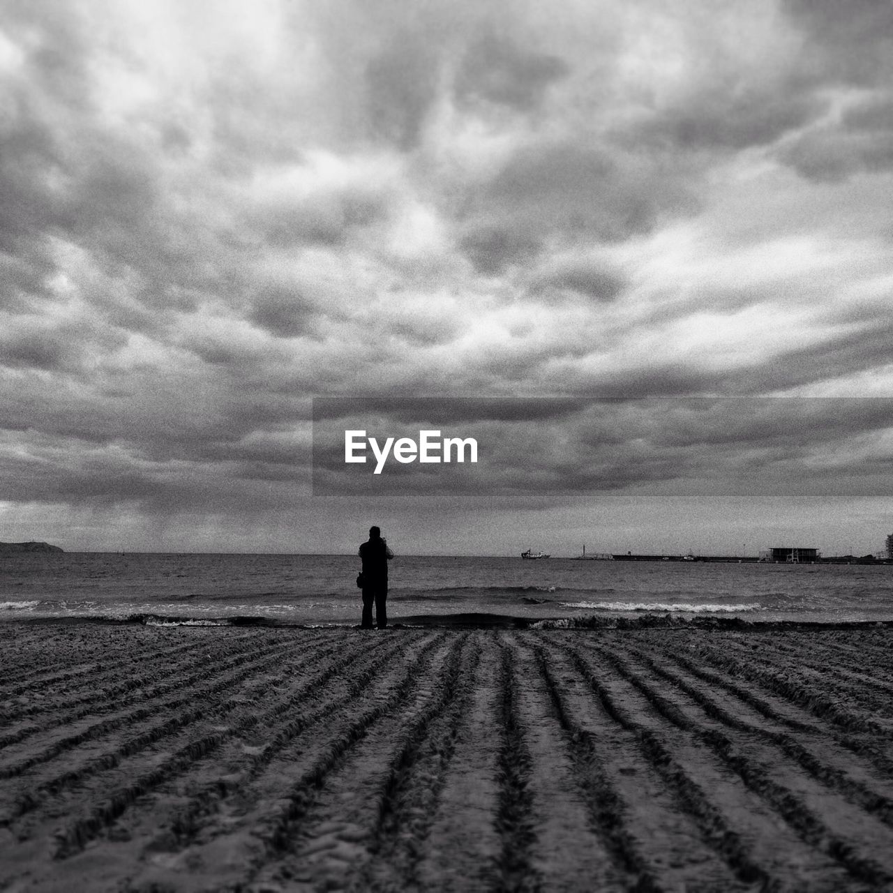 Rear view of man standing at beach against cloudy sky