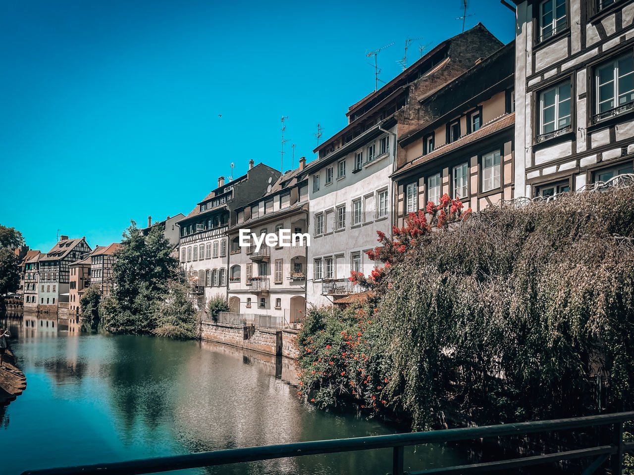 Buildings by river against clear blue sky