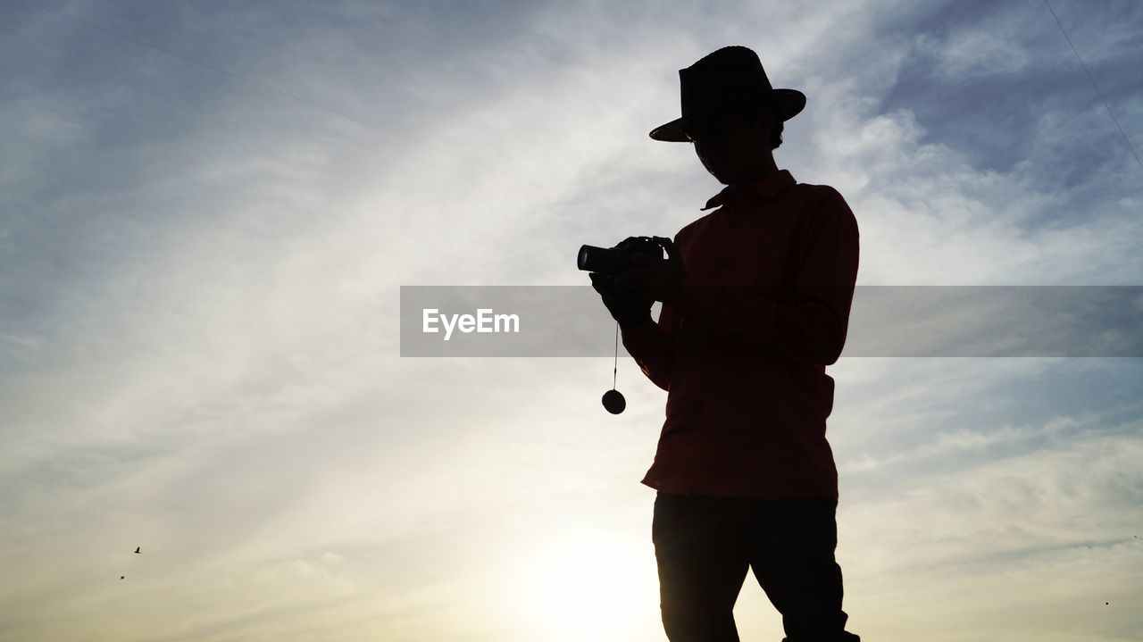 LOW ANGLE VIEW OF MAN HOLDING HAT AGAINST SKY