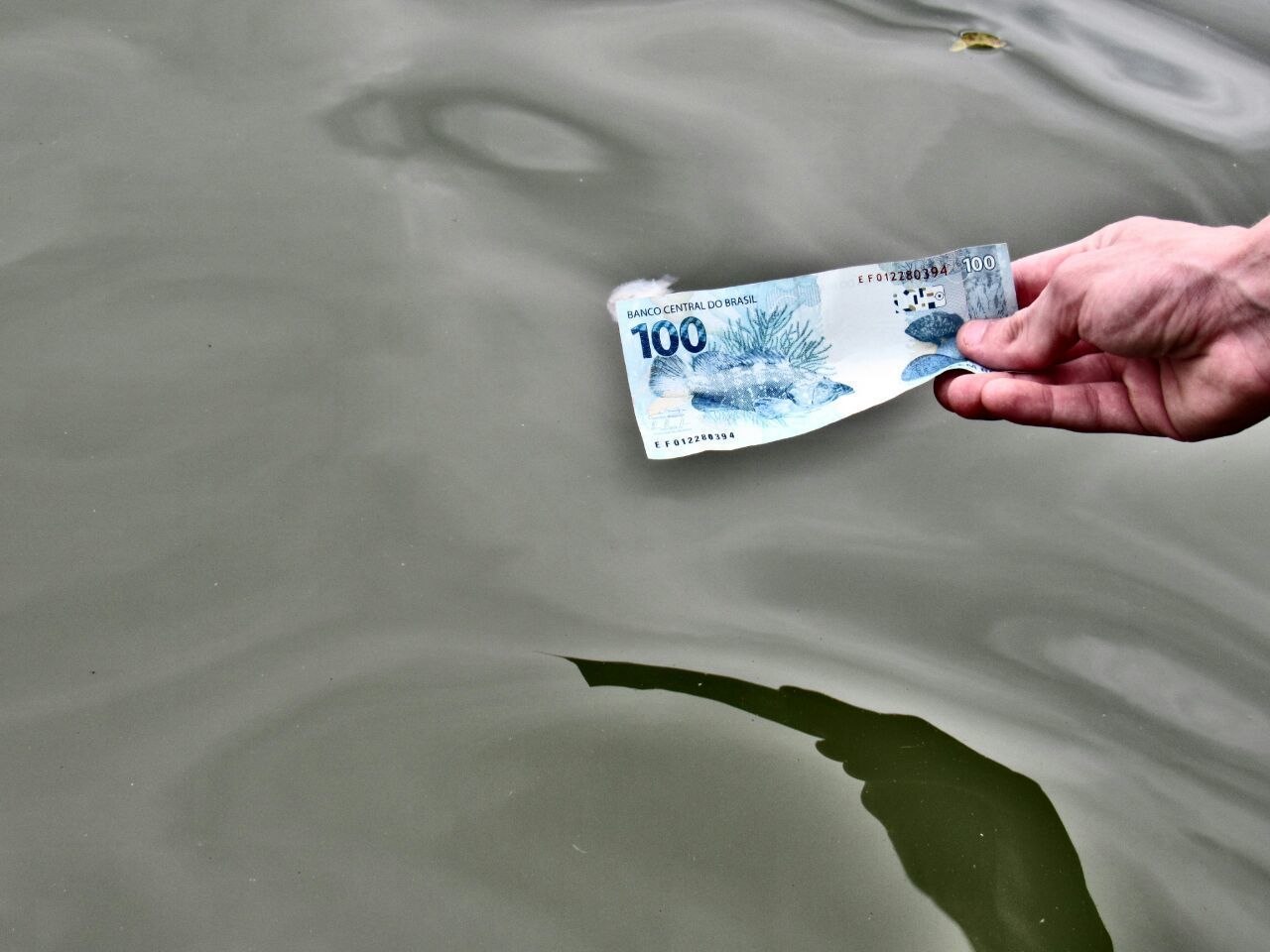 Cropped hand holding paper currency by lake