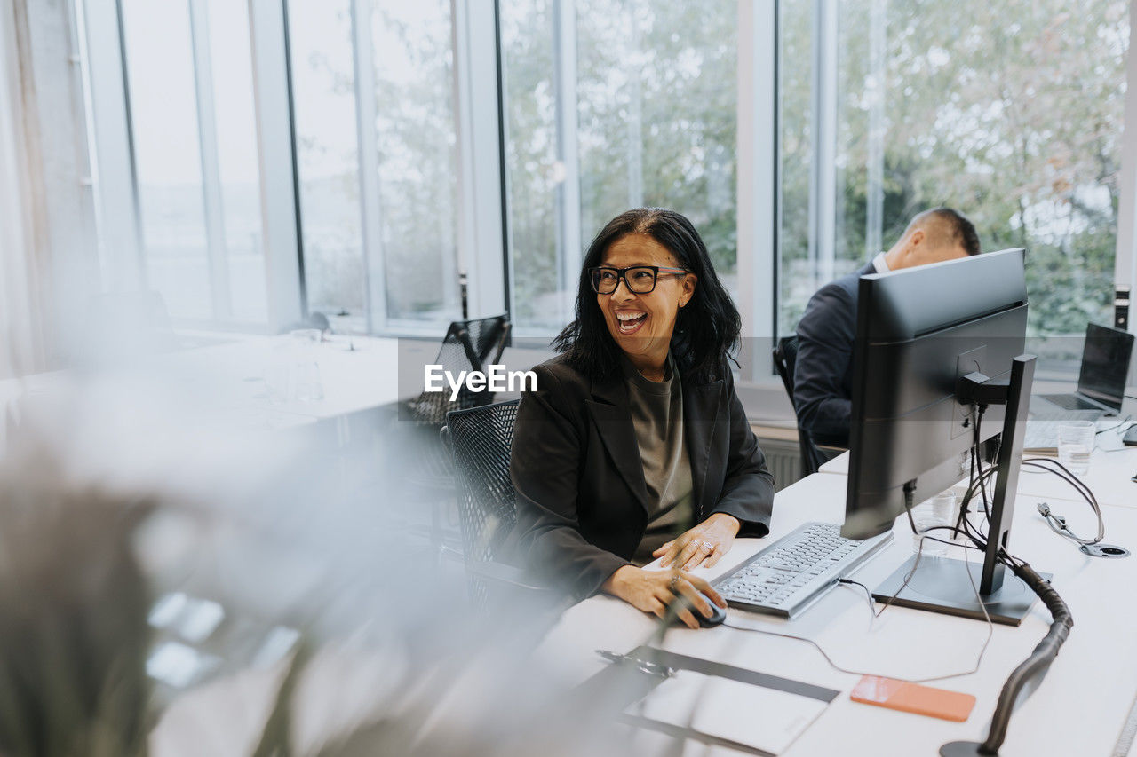 Cheerful senior businesswoman sitting at computer desk while looking away in office