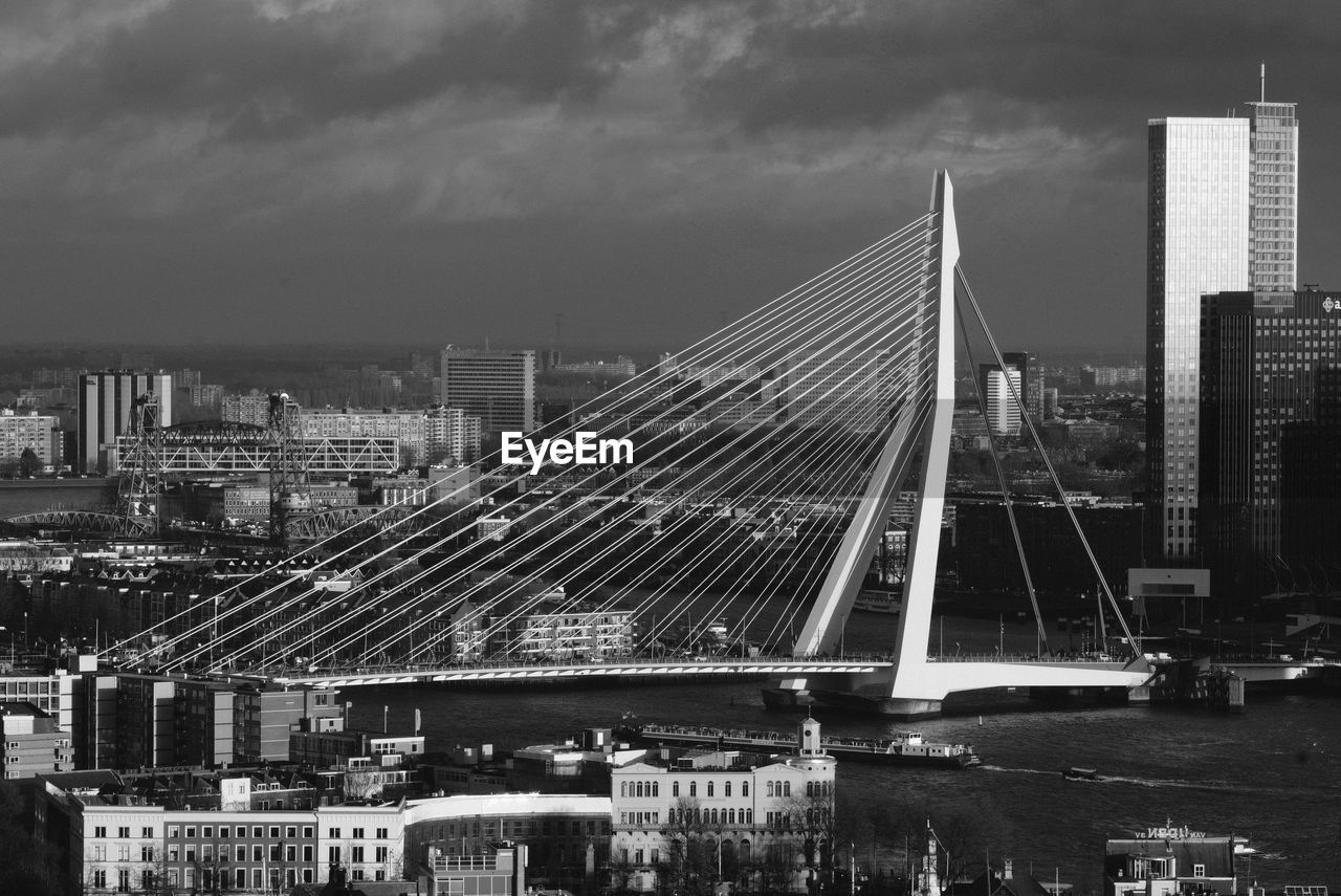 Bridge over river amidst buildings in city against sky