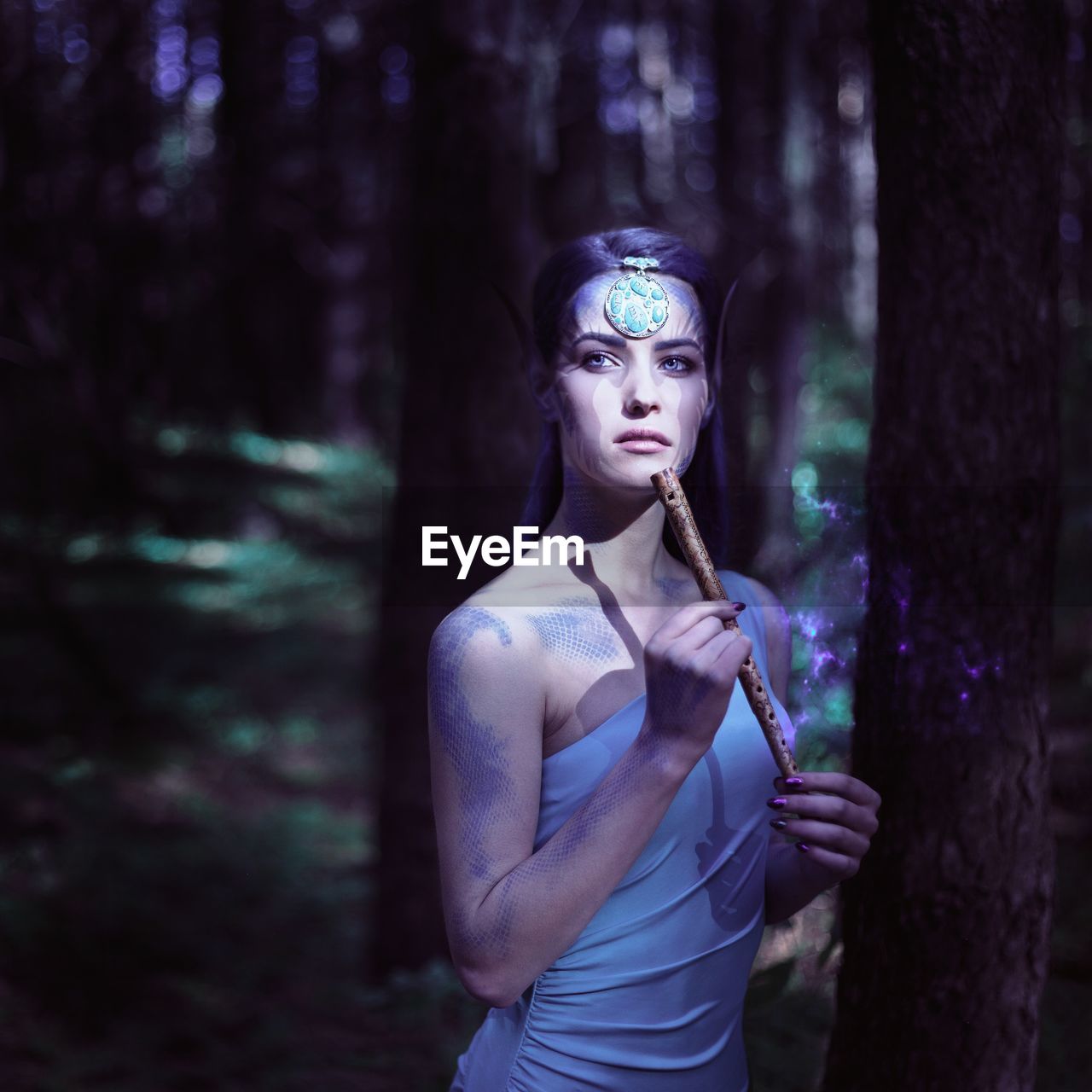 Thoughtful young woman looking away while standing by tree trunk in forest