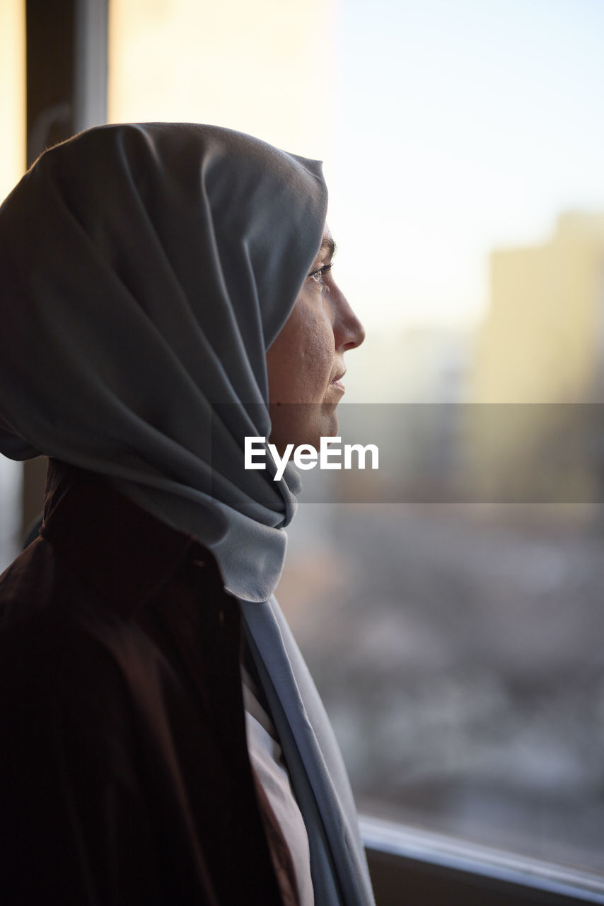 Thoughtful woman in headscarf looking through window