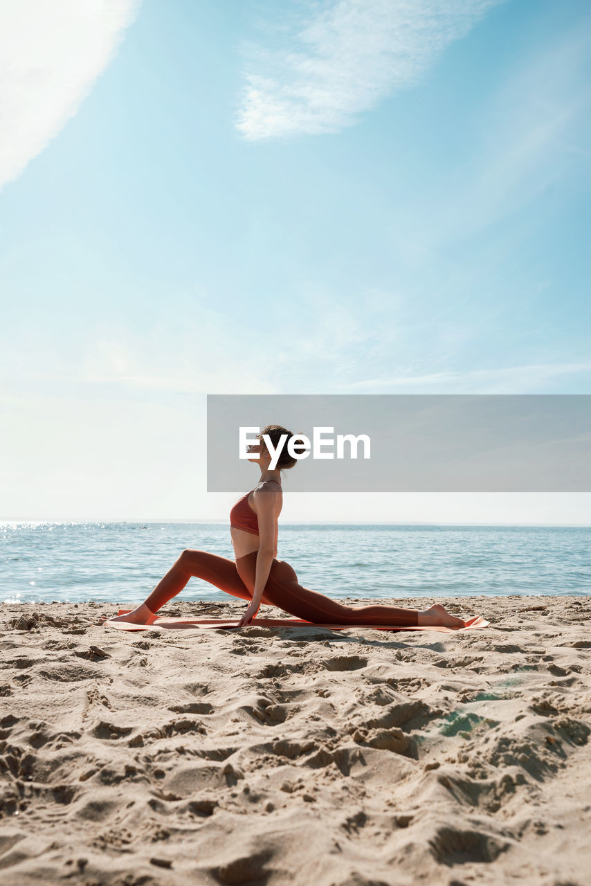 Full length of woman exercising on beach against sky