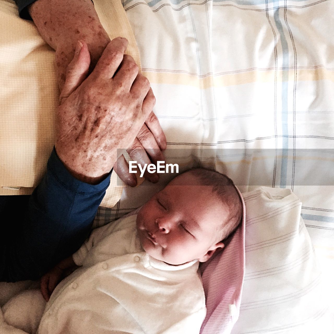 High angle view of person hands by baby sleeping on bed