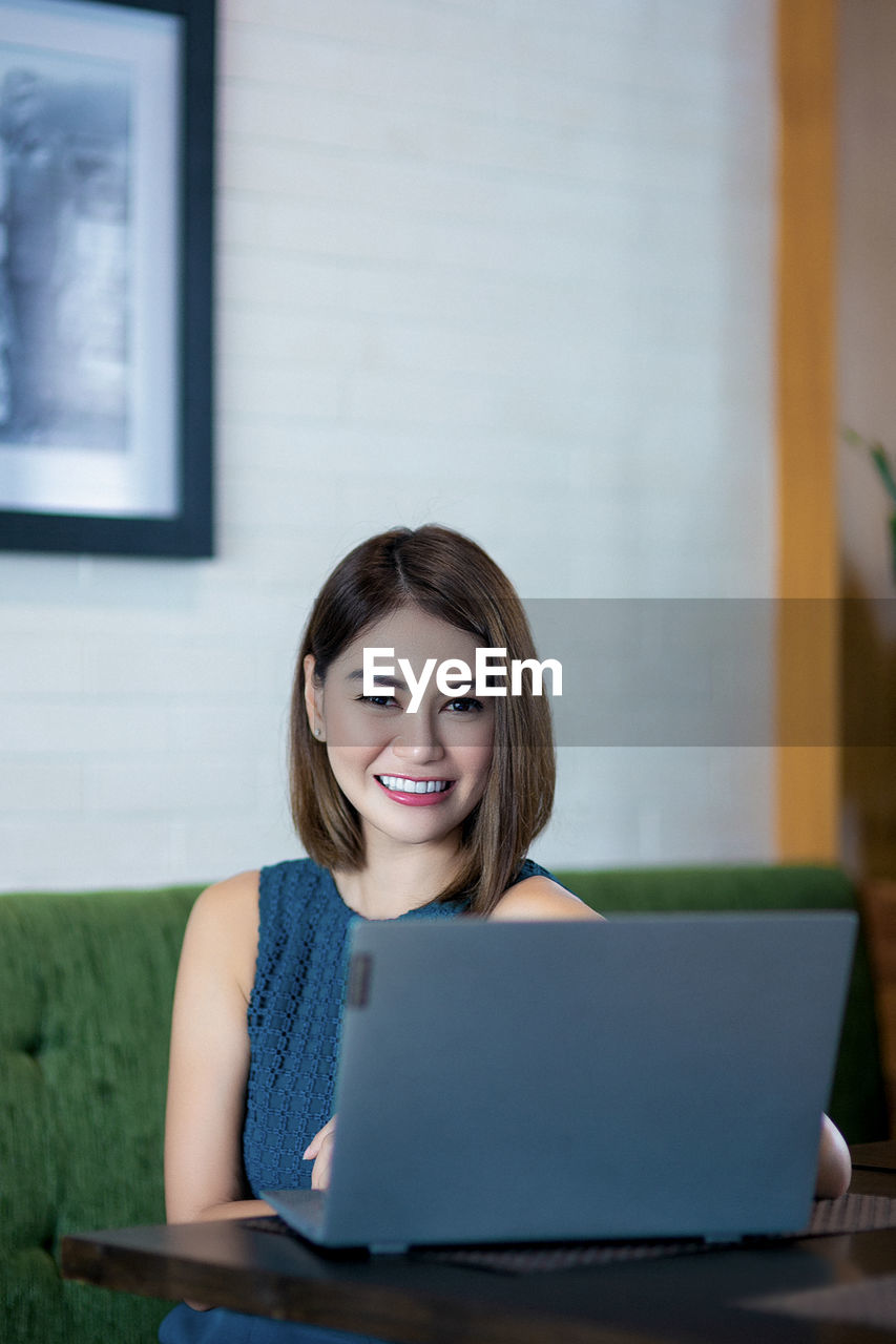 Portrait of smiling young woman using phone while sitting on table