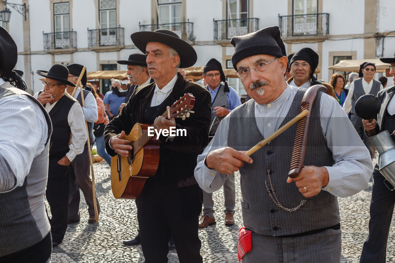 group of people, men, musical instrument, music, architecture, arts culture and entertainment, person, city, musician, crowd, adult, celebration, hat, clothing, event, performance, day, tradition, standing, building exterior, large group of people, street, musical equipment, togetherness, outdoors