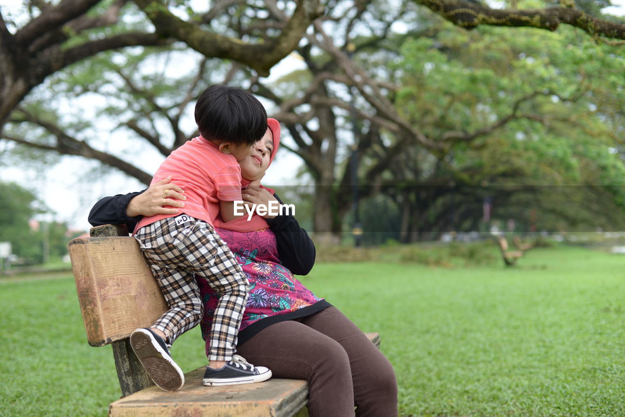 Boy kissing mother sitting on park bench