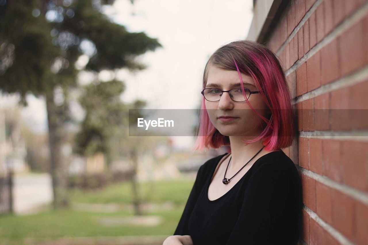 Portrait of teenage girl wearing eyeglasses by brick wall