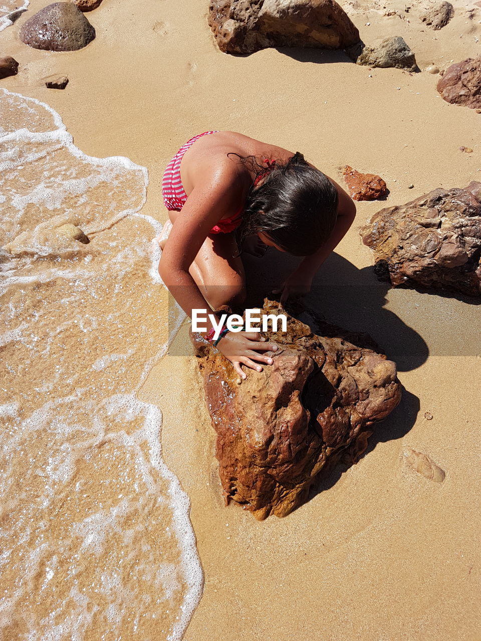 High angle view of girl crouching by rock on shore at beach