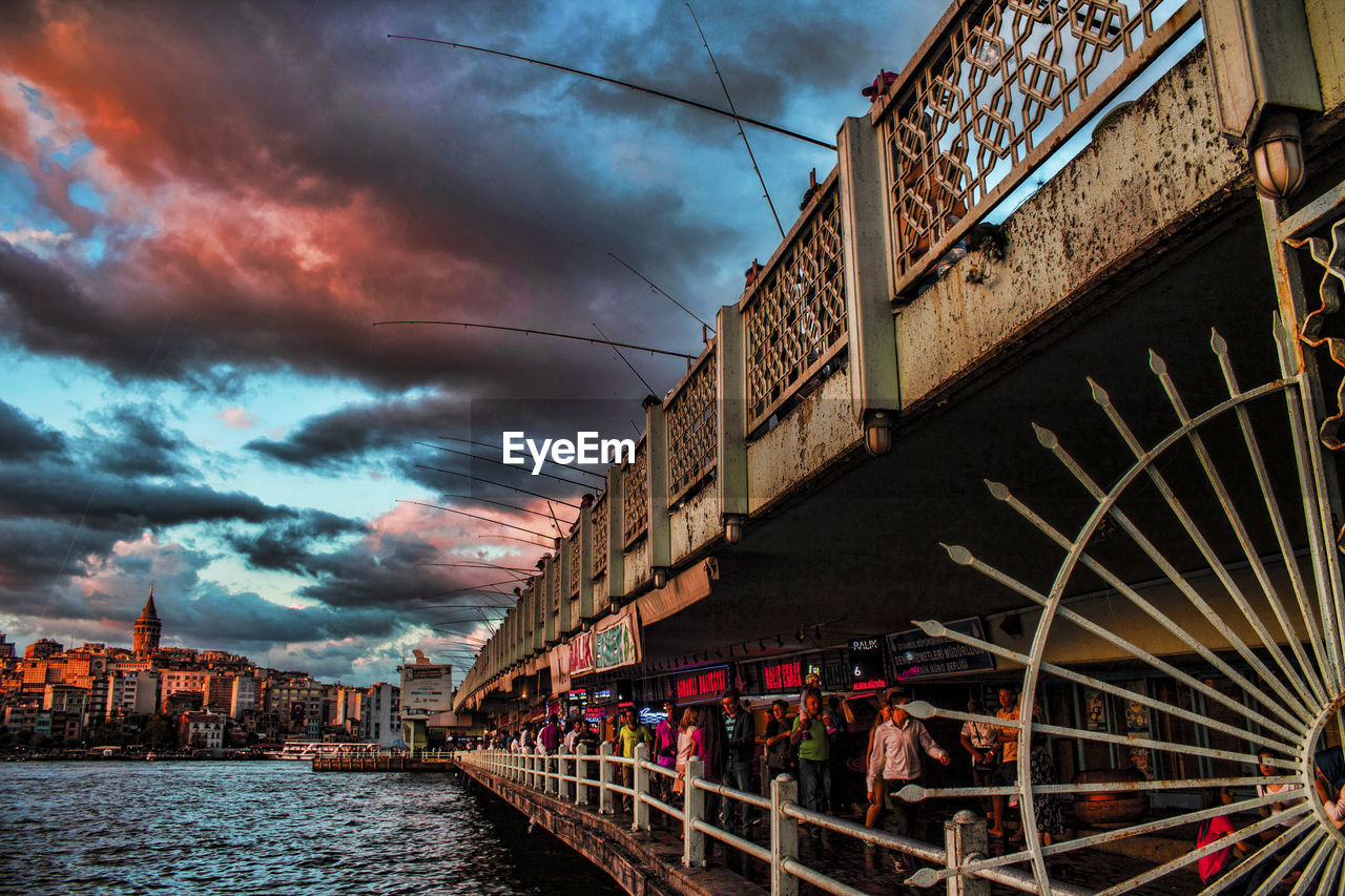 People on walking on building by lake against cloudy sky during sunset