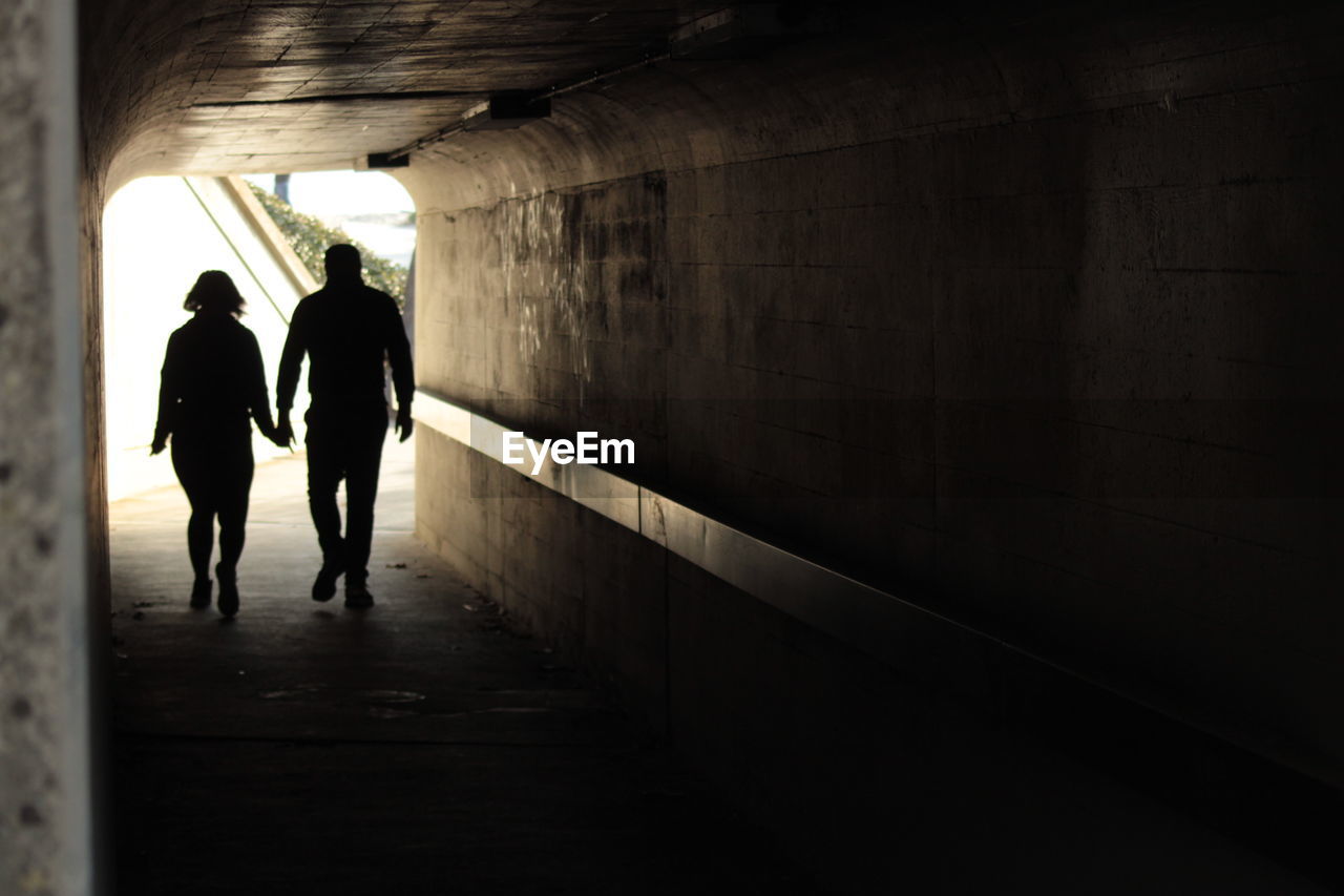 REAR VIEW OF SILHOUETTE COUPLE WALKING IN TUNNEL