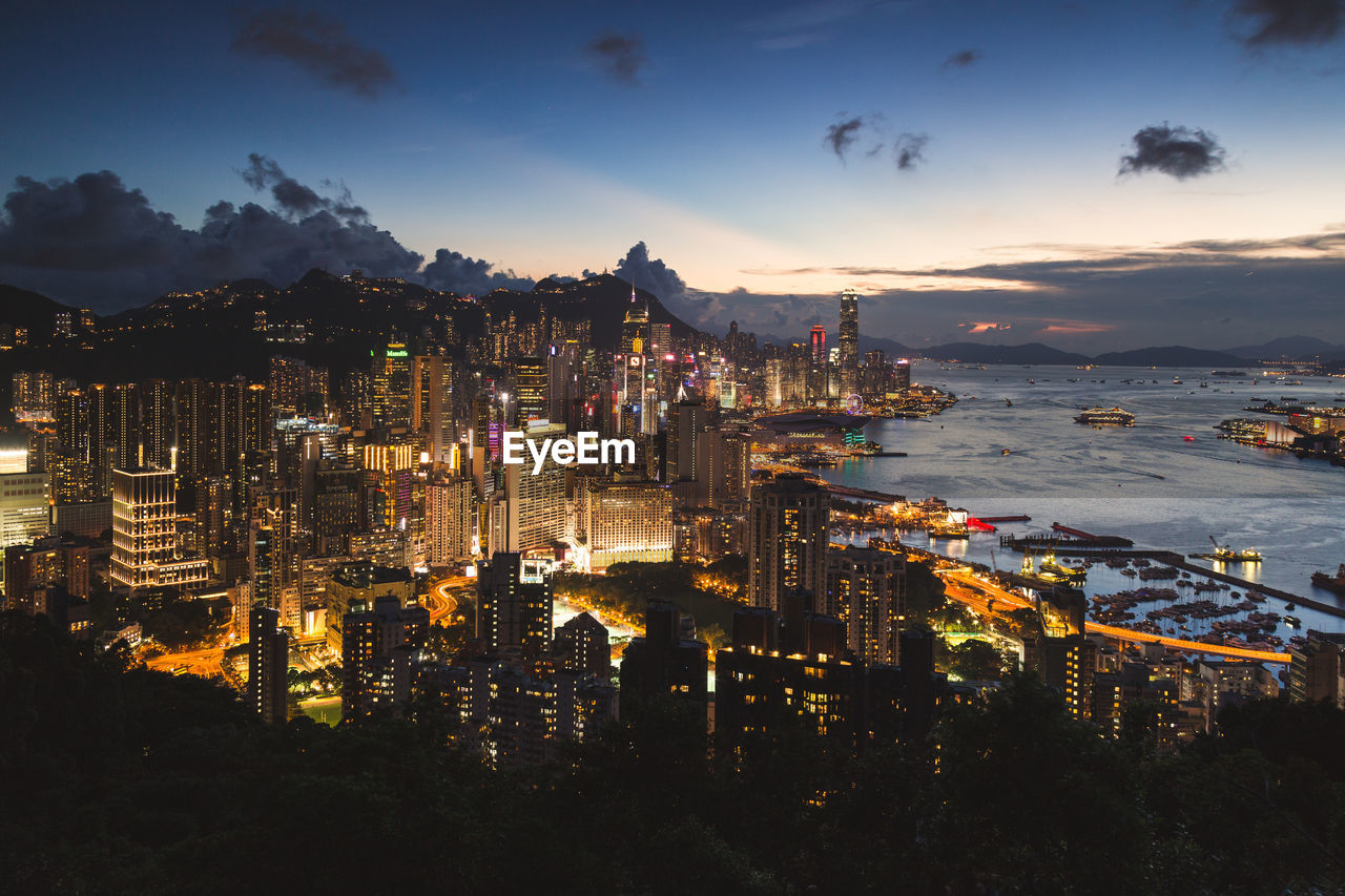 HIGH ANGLE VIEW OF ILLUMINATED CITY BY SEA AT SUNSET