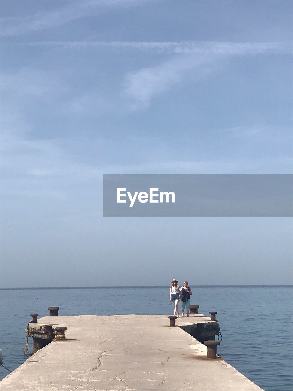 PEOPLE SITTING ON SHORE AGAINST SKY