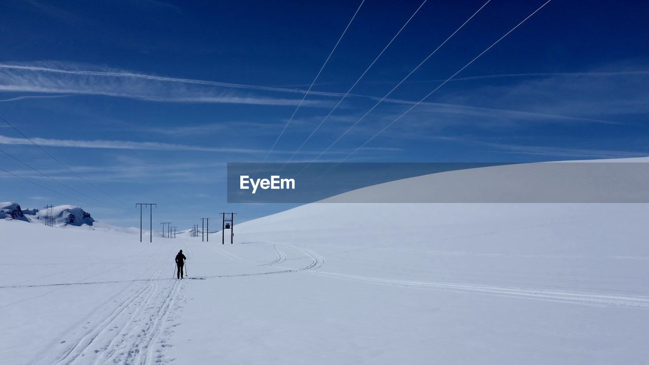 Distance view of person skiing on snowy hill against sky