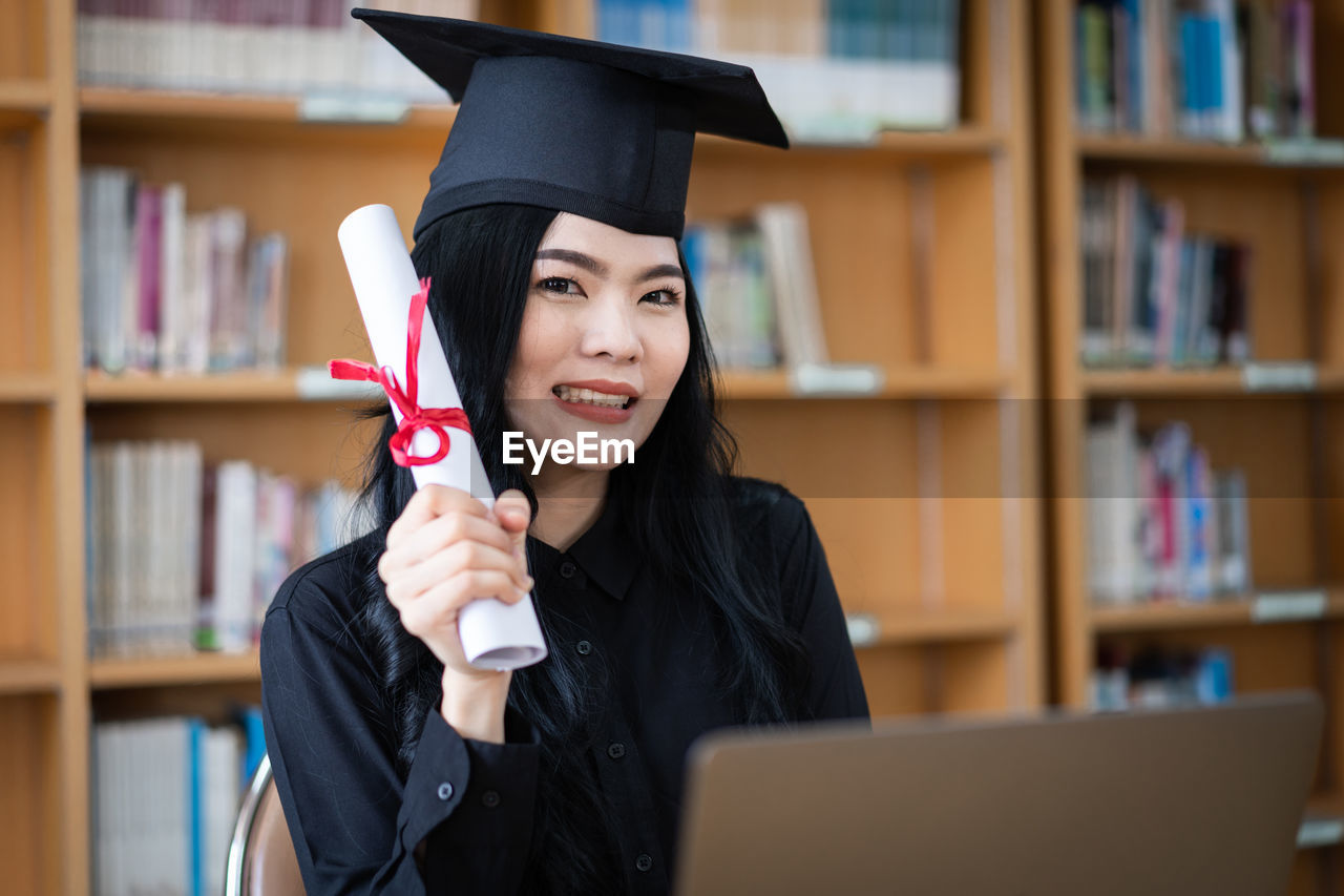 Portrait of student holding diploma at library