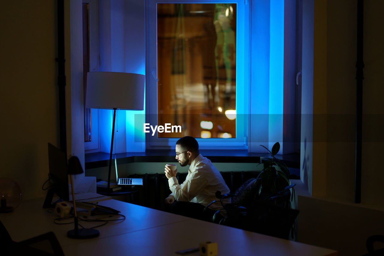 Businessman drink coffee refreshing work on laptop computer in empty office overtime late at night