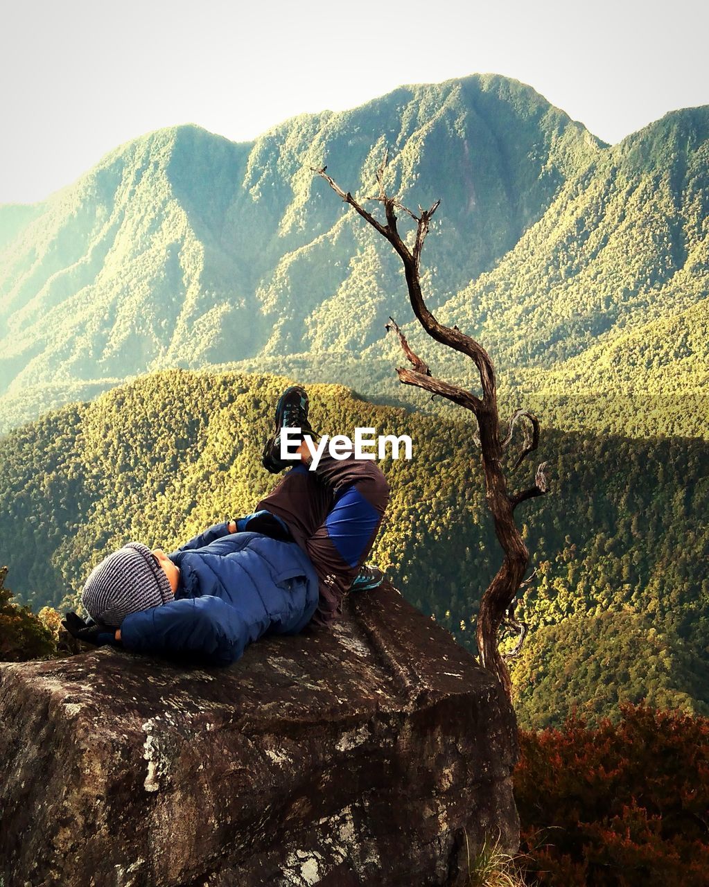 Rear view of man sitting on rock against mountain