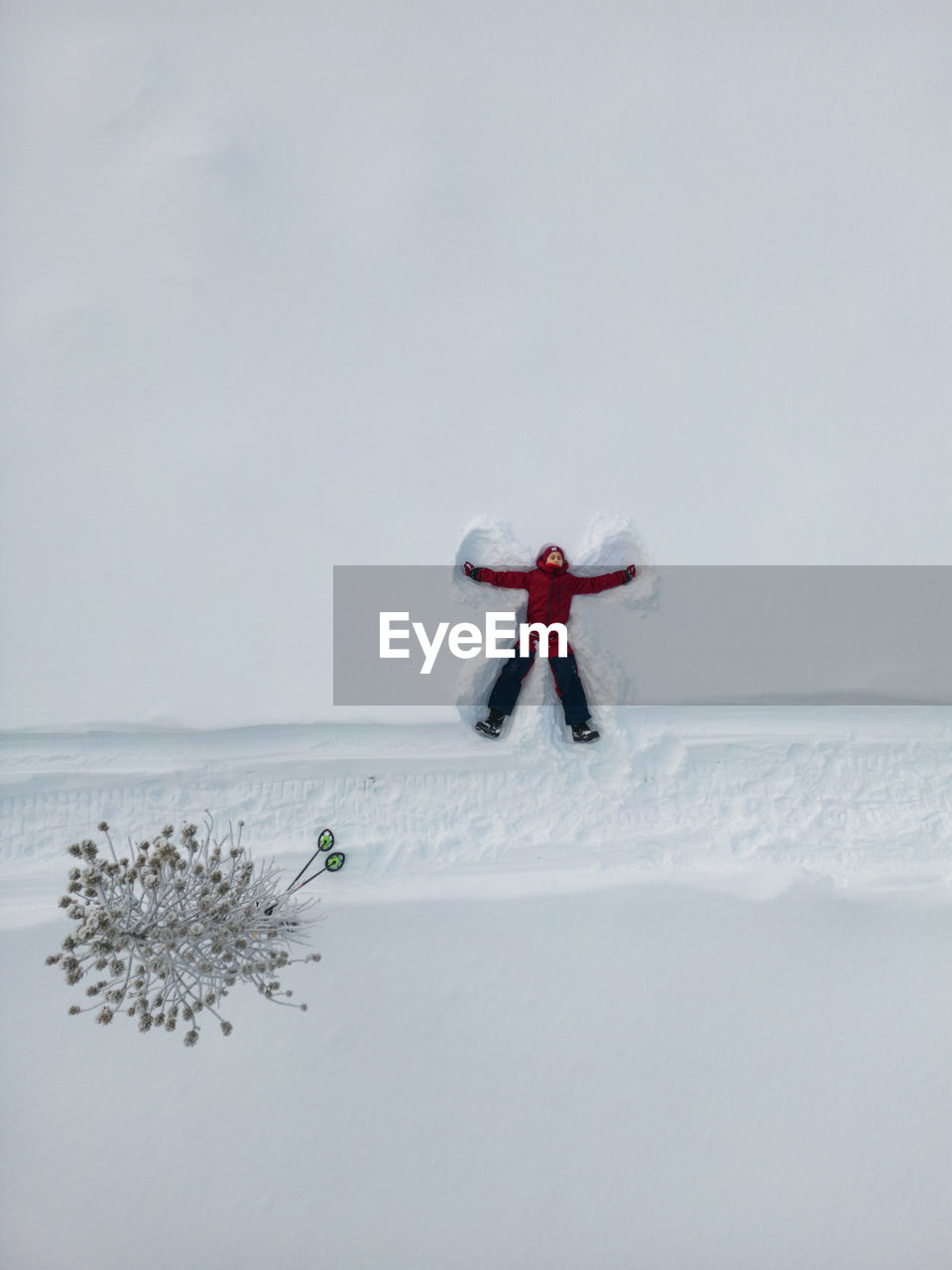 Aerial view of a girl in a red snowsuit playing the angel