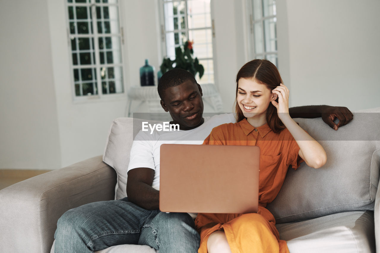 YOUNG COUPLE SITTING ON SOFA AT LAPTOP