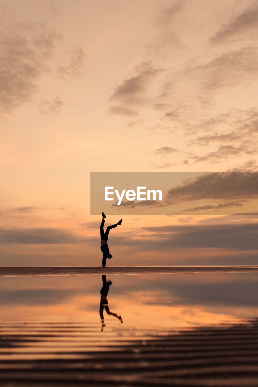 Silhouette man with arms raised against sky during sunset