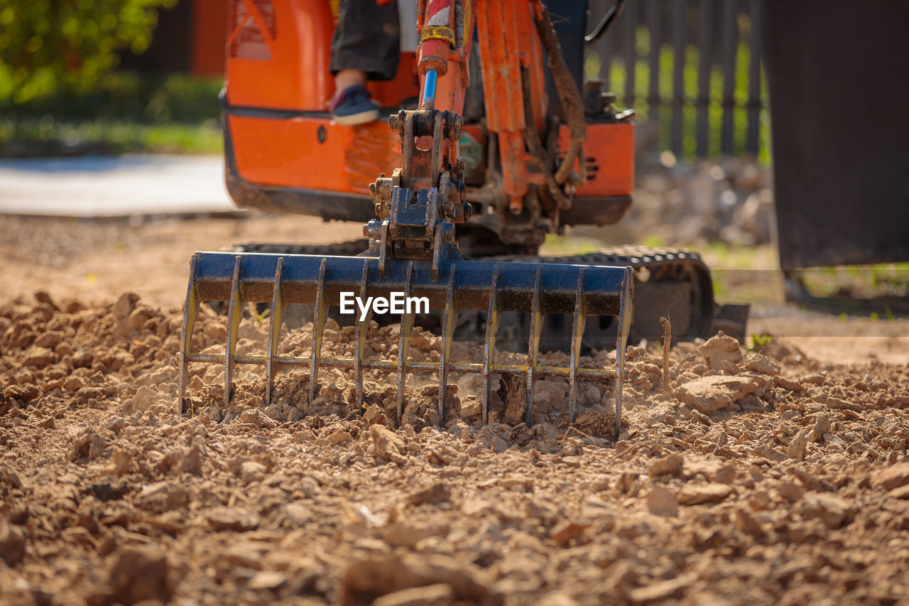 A mini excavator with a rake loosens the ground. landscape preparation
