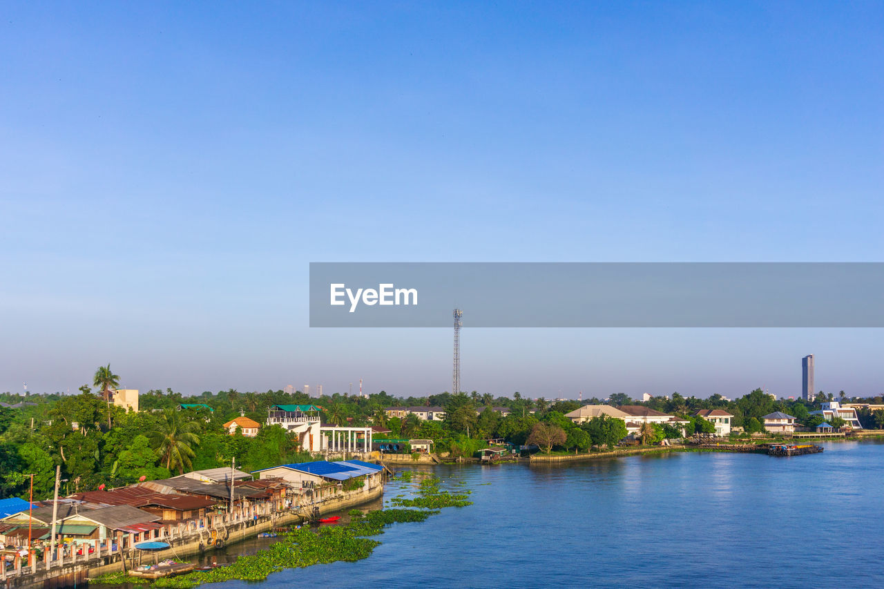 BUILDINGS BY RIVER AGAINST CLEAR BLUE SKY