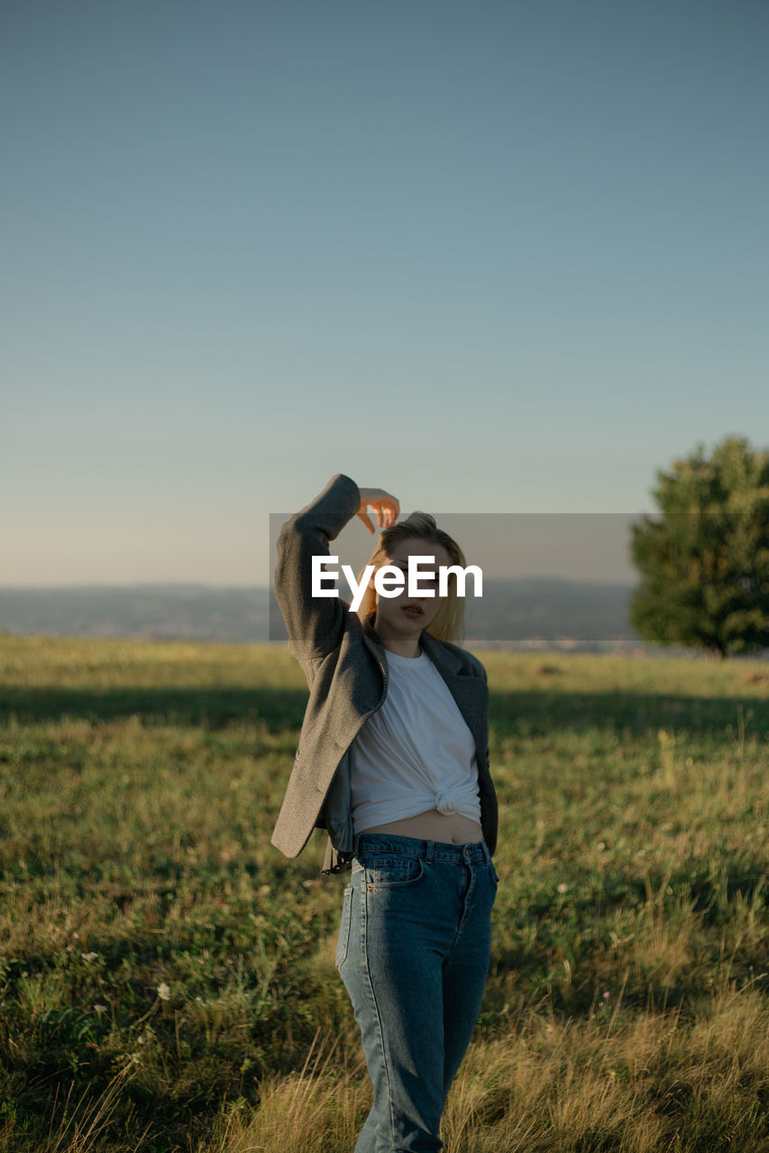 Portrait of a young woman standing in a field during sunset