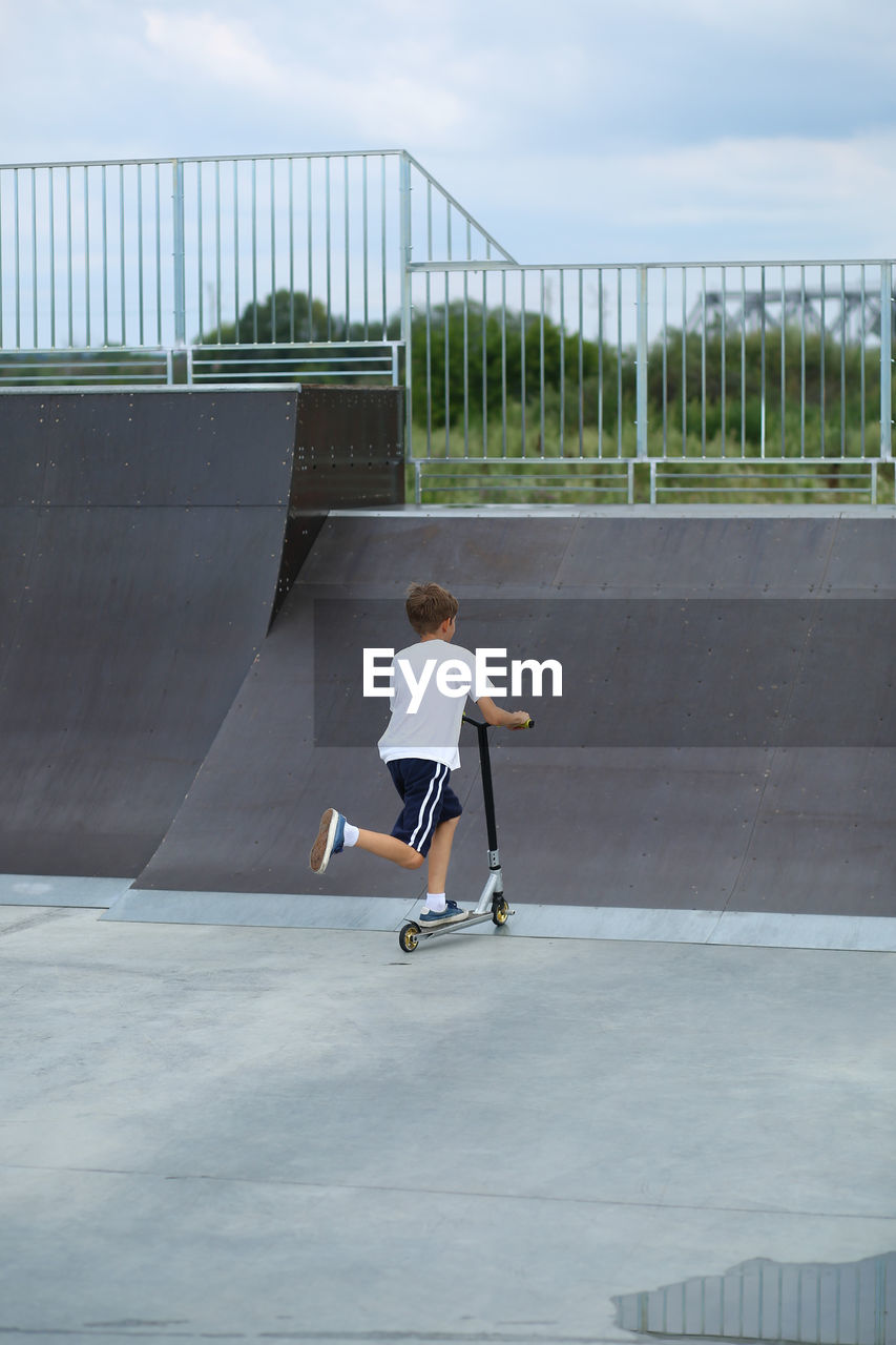 Active ten year old boy riding a scooter in the summer skate park