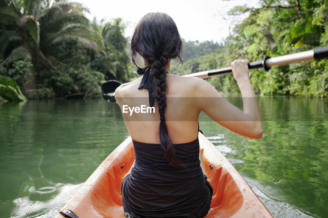 Rear view of woman kayaking on lake at forest