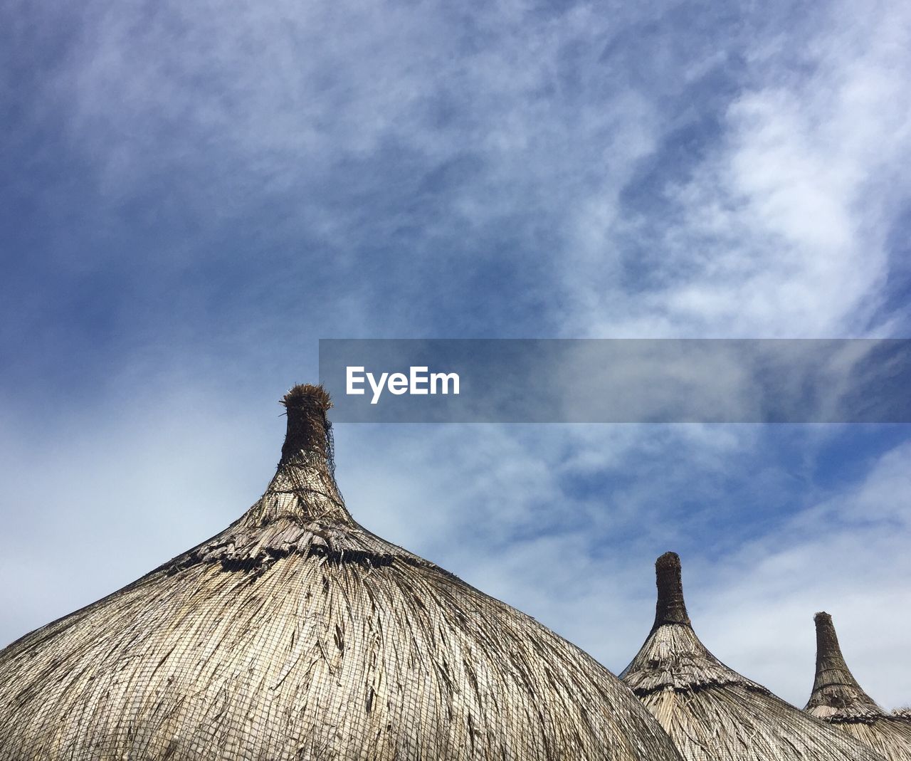 Low angle view of thatched roofs against cloudy sky