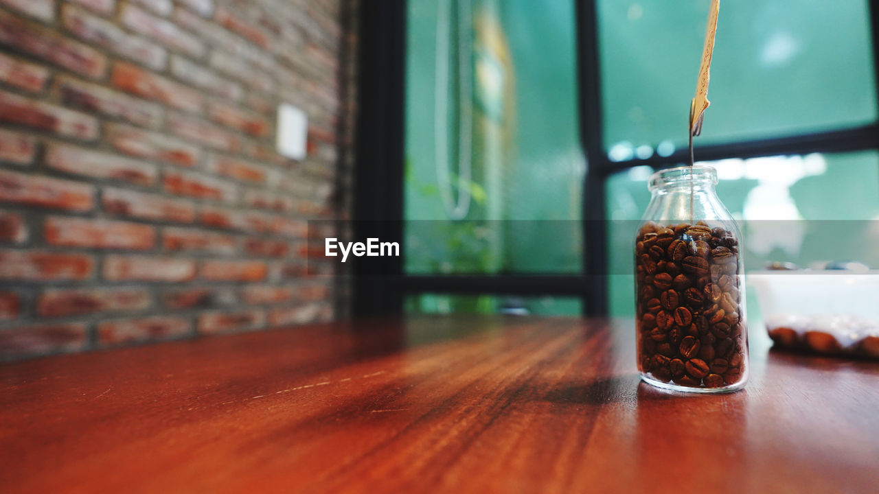 Close-up of glass jar with coffee beans on table against wall