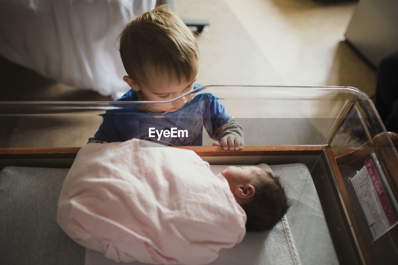High angle view of brother looking at sister sleeping in crib