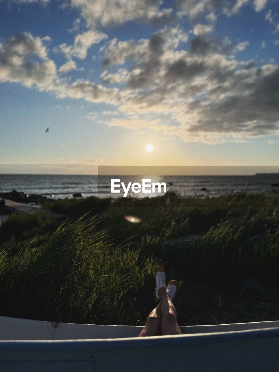 Rear view of woman sitting on beach against sky during sunset