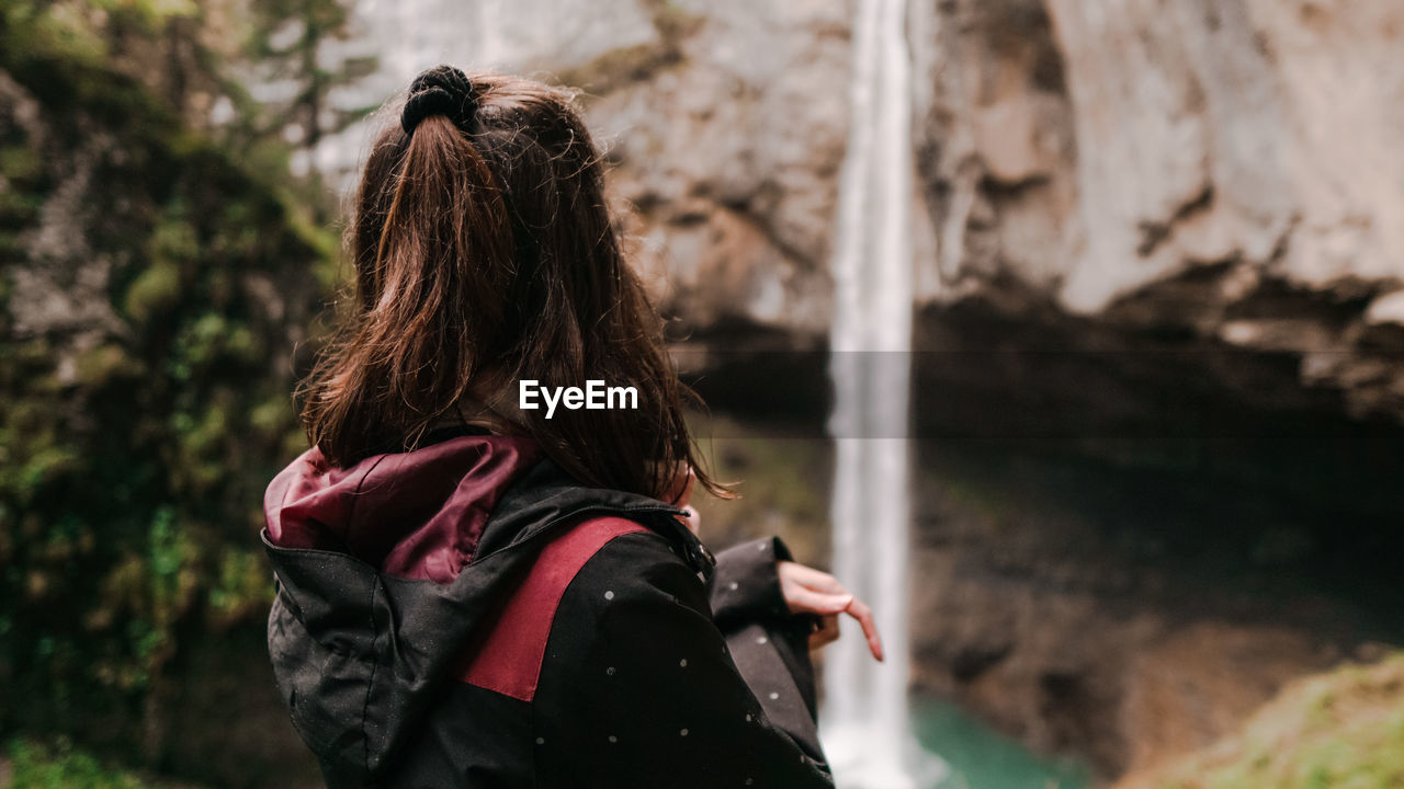 Side view of woman looking at waterfall in forest